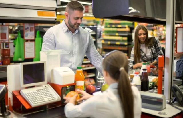 Молодой мужчина и девушка закупают продукты питания на кассе супермаркета