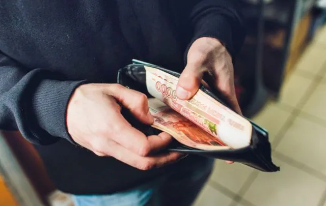 Мужские руки пересчитывают крупные купюры в кошельке