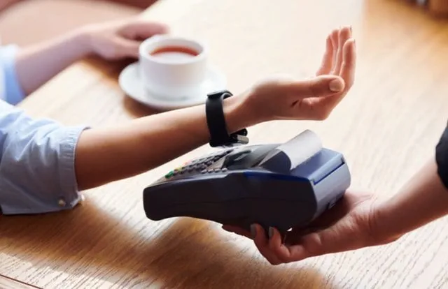 Женская рука с умными часами оплачивает чашку кофе бесконтактным способом