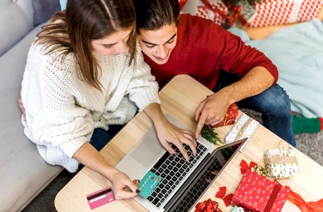 Молодая семейная пара совместно использует кредитную карту через ноутбук для покупки подарков